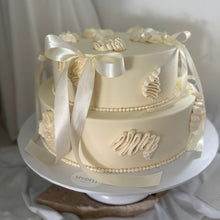 Load image into Gallery viewer, Two-tier buttercream cake with satin ribbons and bow detailing in soft ivory tones