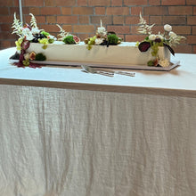 Load image into Gallery viewer, Long rectangular table with a white tablecloth against a brick wall.