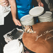 Load image into Gallery viewer, Table setting with plates, cutlery, and a cake with 'Just Married' inscription at a wedding reception.