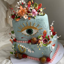Load image into Gallery viewer, Custom sculptural evil eye cake with floral, fruit, and gold detailing, photographed as a vintage inspired statement cake centrepiece.
