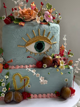 Load image into Gallery viewer, Two tier sculptural evil eye cake with hand made sugar florals, fruit accents, gold details, and textured ganache, styled as a statement cake.