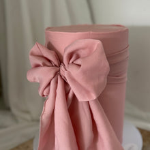 Load image into Gallery viewer, Close-up of a soft pink bow detail on a tall single tier cake with smooth buttercream finish