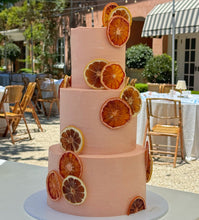 Load image into Gallery viewer, Three-tier Euro summer hues cake with dried citrus in an outdoor wedding setting
