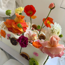Load image into Gallery viewer, Description: Full view of Spodeli’s rectangular Floral Chaos Slab Cake, decorated with colourful seasonal flowers, vintage piping, pearls and dried citrus.
