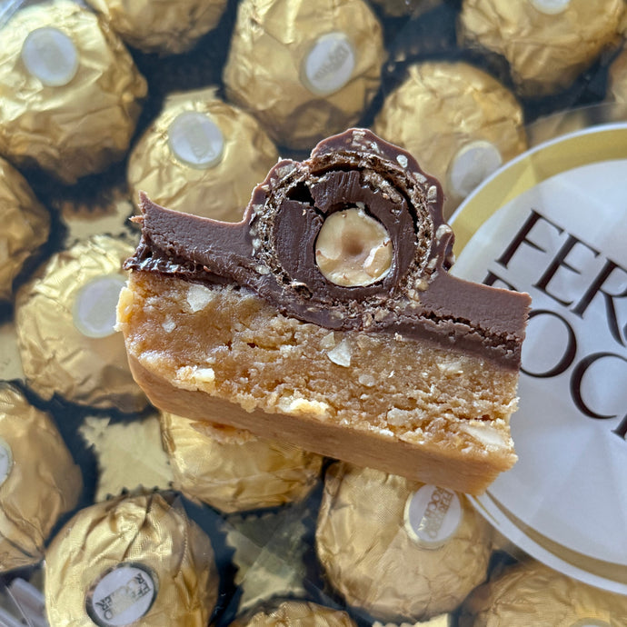 Close-up of a Ferrero Rocher chocolate with a box of Ferrero Rocher chocolates in the background.