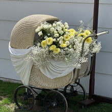 Load image into Gallery viewer, Vintage-style pram decorated with white and yellow flowers against a white wall.
