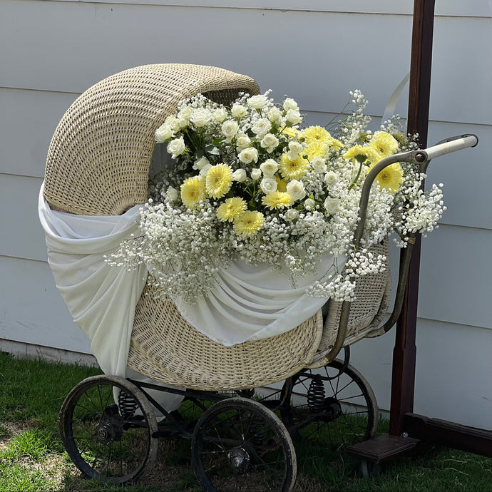 Vintage-style pram decorated with white and yellow flowers against a white wall.