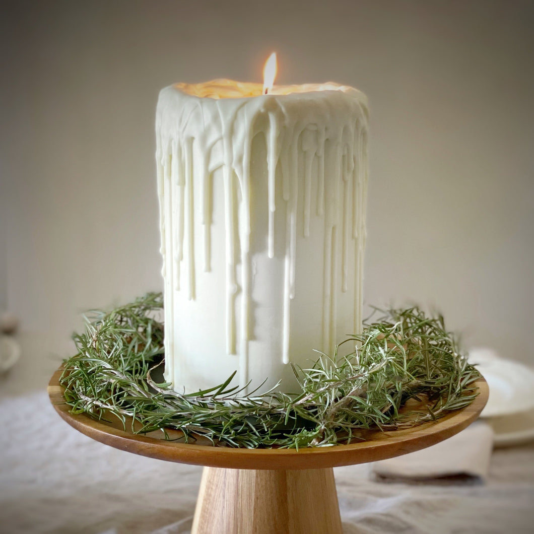 White candle on a wooden stand with greenery, set against a neutral background