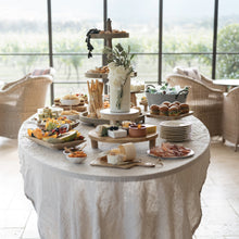 Load image into Gallery viewer, Smooth white ethereal cake with fresh florals surrounded by a curated dessert table
