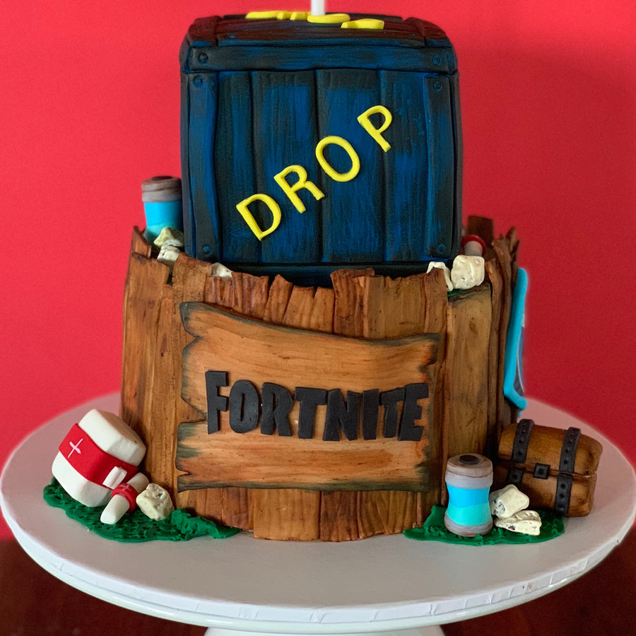 Front view of a hand-sculpted Fortnite supply drop cake with wooden crate top tier and timber fence base by Spodeli 