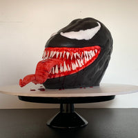 Side view of a three-dimensional sculpted Venom cake by Spodeli displayed on a cake stand
