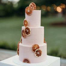 Load image into Gallery viewer, Side view of a three-tier cake with warm summer tones and citrus accents
