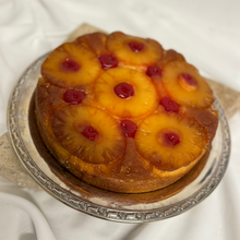 Load image into Gallery viewer, An upside down pineapple cake with caramelized pineapple slices and maraschino cherries on top, served on a silver platter.
