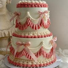Load image into Gallery viewer, Three-tiered cake with pink and white ruffles and bows on a neutral background
