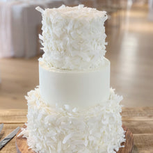 Load image into Gallery viewer, A three-tier white wedding cake decorated with coconut flakes
